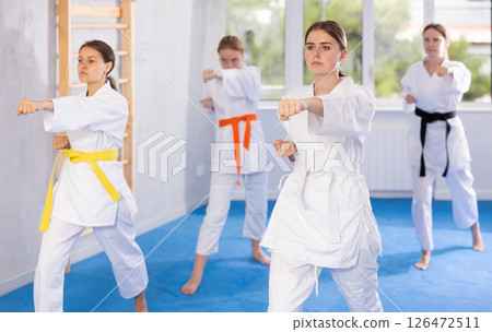 Teenage girl with group in kimonos performing kata to hone martial arts skills Teenage girl with group in kimonos performing kata to hone martial arts skills 126472511