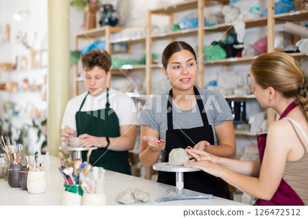 Potter helps young apprentices mold pottery from clay in workshop 126472512