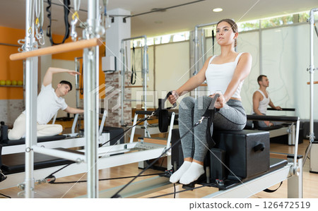 Girl performing pulling straps exercise on Pilates reformer with box Girl performing pulling straps exercise on Pilates reformer with box 126472519
