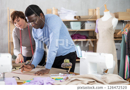 Two dressmakers sketching garment pattern on paper in sewing studio Two dressmakers sketching garment pattern on paper in sewing studio 126472520