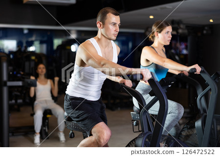 Sportive young couple doing air bike exercises in well-equipped gym 126472522
