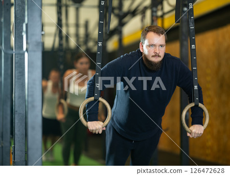 Sportive young guy working out with gymnastic rings in gym during crossfit workout 126472628