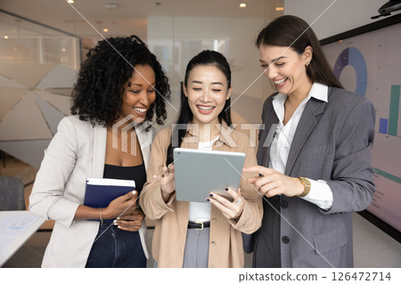 Three multiethnic businesswomen standing in office using digital tablet 126472714
