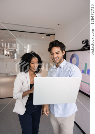 Two multiethnic young 30s professional teammates working together using laptop 126472739