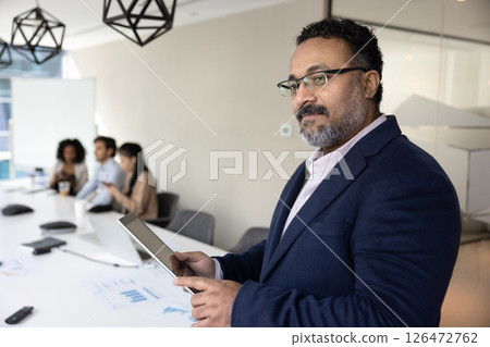 Indian businessman standing in meeting room using his digital tablet Indian businessman standing in meeting room using his digital tablet 126472762