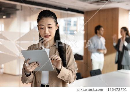 Focused Vietnamese businesswoman working on tablet device standing in boardroom 126472791