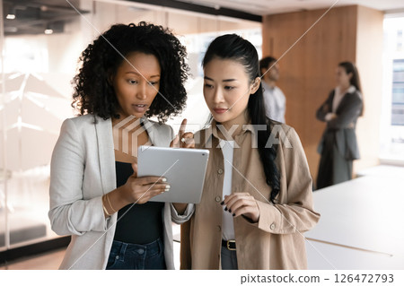 Serious African and Vietnamese women teammates using tablet in office 126472793