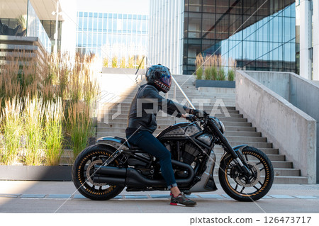 Handsome motorcyclist with helmet sitting on his moto against urban backdrop 126473717