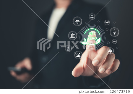 A person touches a glowing net zero icon surrounded by symbols of sustainability and ecology, representing environmental goals, renewable energy, and efforts for a greener and cleaner future. 126473719