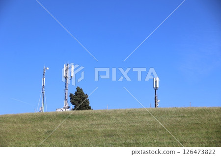 Three tall towers with antennas on top of them are standing in a grassy field 126473822