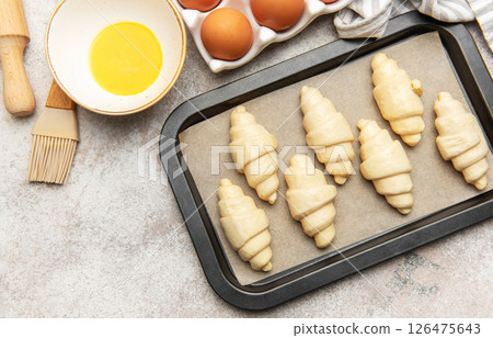 Baker preparing raw croissants on baking tray for baking Baker preparing raw croissants on baking tray for baking 126475643