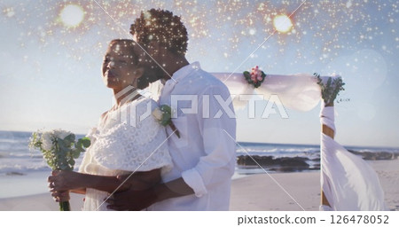 Image of light spots over biracial married couple embracing at seaside 126478052