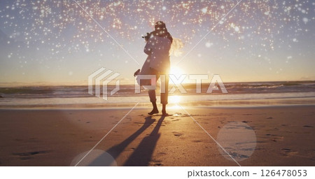 Image of light spots over biracial married couple embracing at seaside 126478053