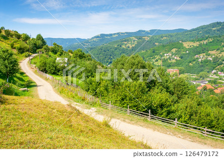 rural landscape with road in summer. countryside nature with mountain in background. rustic scenery with green grass on hill and blue sky. scenic view of gravel ground street in valley rural landscape with road in summer. countryside nature with mountain in background. rustic scenery with green grass on hill and blue sky. scenic view of gravel ground street in valley 126479172