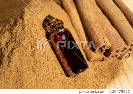 Glass bottle of cinnamon oil on the background of cinnamon sticks and ground cinnamon. 126479957