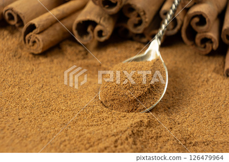 Close-Up of Spoonful of Brown Ground Spice and Cinnamon Sticks. Natural Food Scene. 126479964