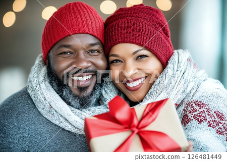Smiling african adult couple in winter clothing holding gift box with red bow 126481449
