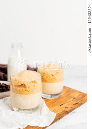 Iced or frappe coffee smoothie on a glass cup and Roasted coffee beans, and milk on marble backdrop. Copy space for your text. vertical photo 126482204