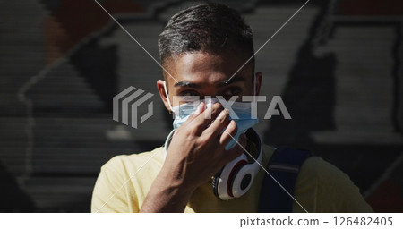 Biracial man with headphones putting on face mask in the street Biracial man with headphones putting on face mask in the street 126482405