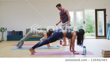 Diverse group practicing yoga pose in class with male instructor helping Diverse group practicing yoga pose in class with male instructor helping 126482465