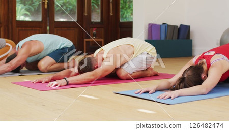Diverse group in yoga position stretching on mats during yoga class at health studio Diverse group in yoga position stretching on mats during yoga class at health studio 126482474