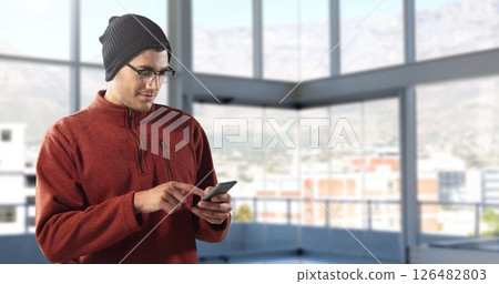 Man in beanie using smartphone in modern office with large windows Man in beanie using smartphone in modern office with large windows 126482803
