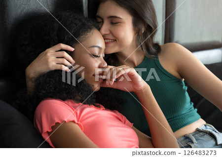 Happy lesbian couple hugging and laughing on bed in bedroom. Lesbian multiethnic couple enjoying the company of each other at home. 126483273