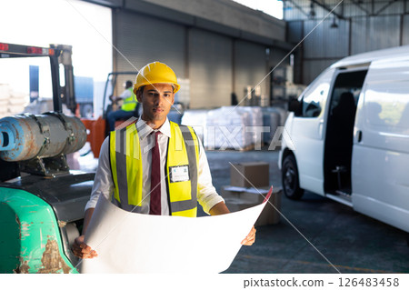 Warehouse worker in safety gear examining blueprint near delivery van Warehouse worker in safety gear examining blueprint near delivery van 126483458