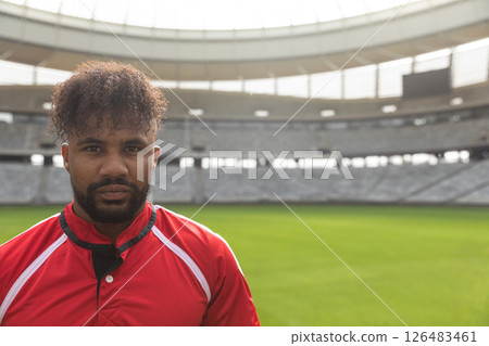 Rugby player in red jersey standing confidently in empty stadium, copy space 126483461