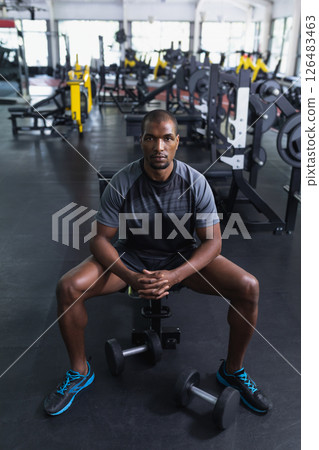 Athletic man sitting on bench in gym, preparing for workout with dumbbells 126483463
