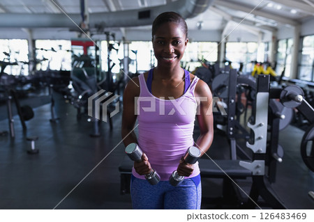African American woman lifting dumbbells in gym, smiling confidently during workout 126483469