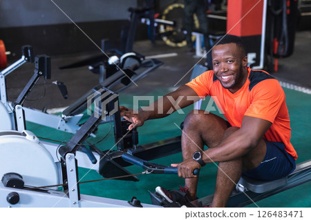 Man in orange shirt using rowing machine at gym, smiling and enjoying workout 126483471