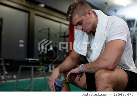 Exercising at gym, man resting with towel and water bottle, looking focused, copy space 126483475