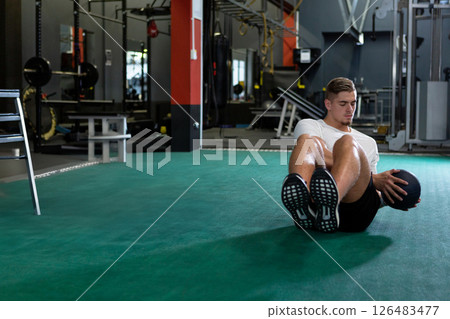 Man exercising with medicine ball on gym floor, focusing on core strength, copy space 126483477