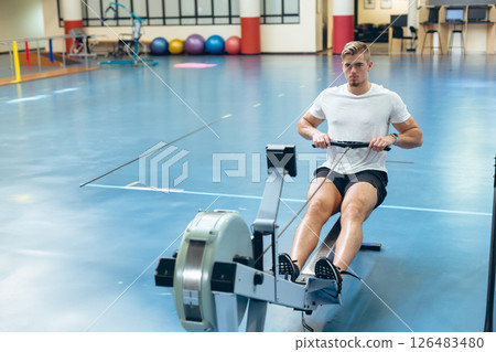 Man exercising on rowing machine in gym, focused on fitness routine, copy space Man exercising on rowing machine in gym, focused on fitness routine, copy space 126483480