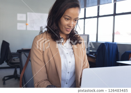 In office, businesswoman concentrating on work while using laptop at desk 126483485