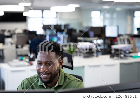 Smiling man working at office desk, focusing on computer screen, copy space 126483511