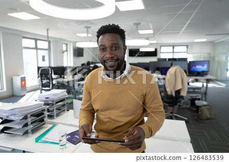 Using tablet, businessman surrounded by documents and computers in modern office 126483539