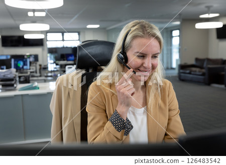 Blonde woman in office using headset, smiling while assisting customer 126483542
