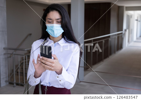 Businesswoman wearing mask using smartphone in office hallway, staying connected Businesswoman wearing mask using smartphone in office hallway, staying connected 126483547