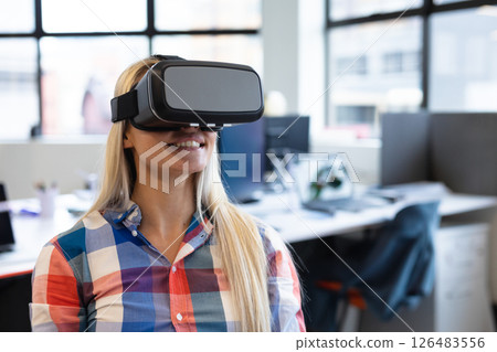 Smiling woman using VR headset in modern office, exploring virtual reality 126483556