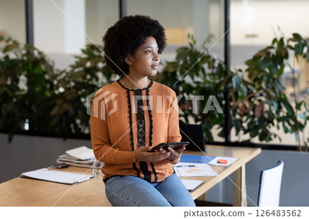 African American woman holding tablet, thoughtfully looking away in modern office 126483562