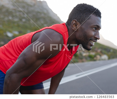 Athletic man in red tank top resting after outdoor run on mountain road 126483563