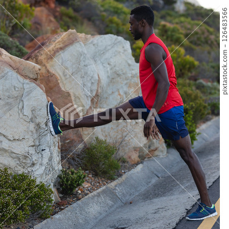 Athletic man stretching leg on rock during outdoor workout in nature Athletic man stretching leg on rock during outdoor workout in nature 126483566