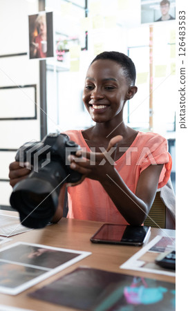 African American woman holding camera at office desk, smiling and reviewing photos 126483583