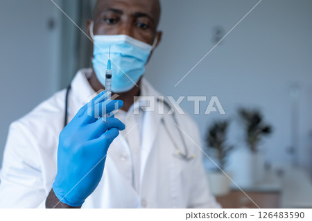 Doctor wearing mask and gloves holding syringe, preparing for vaccination 126483590