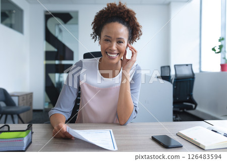 African American woman smiling at office desk holding document, looking confident African American woman smiling at office desk holding document, looking confident 126483594