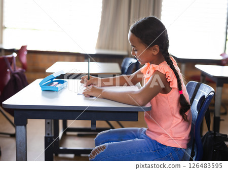 In school, young girl writing in notebook at desk, concentrating on task In school, young girl writing in notebook at desk, concentrating on task 126483595
