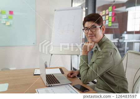 Businessman in office smiling at camera with laptop and smartphone on desk, copy space Businessman in office smiling at camera with laptop and smartphone on desk, copy space 126483597