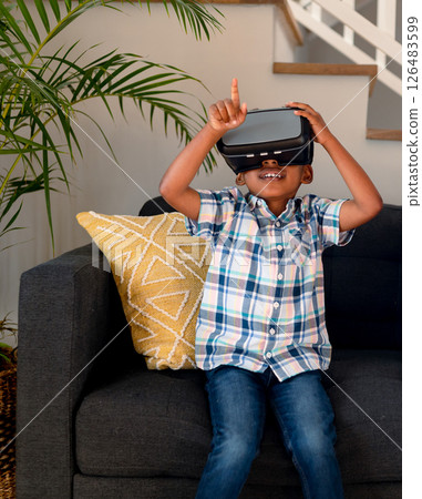 African American boy enjoying virtual reality headset while sitting on couch at home 126483599